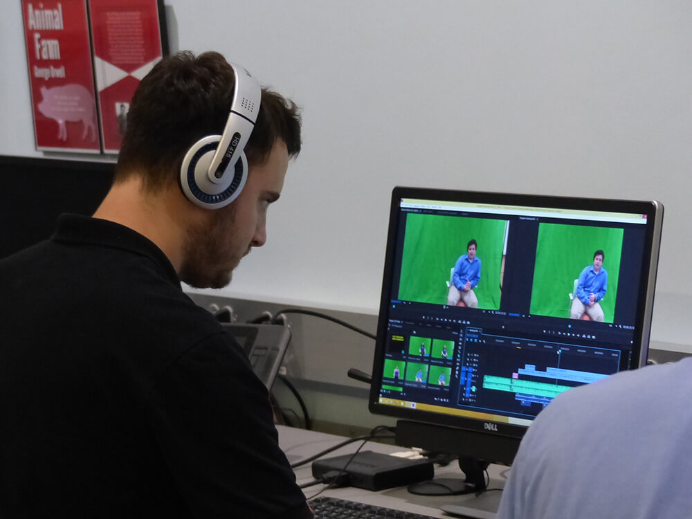 Photo of a student editing video using a green screen or chroma key effect in the CIT (Computer Information Technology) lab in the Lyons Center Social Media