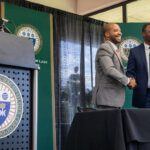 Photo of Modesto Montero shaking hands with Elms College's president Harry E. Dumay after signing the paperwork at the event