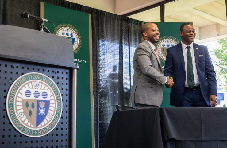 Photo of Modesto Montero shaking hands with Elms College's president Harry E. Dumay after signing the paperwork at the event