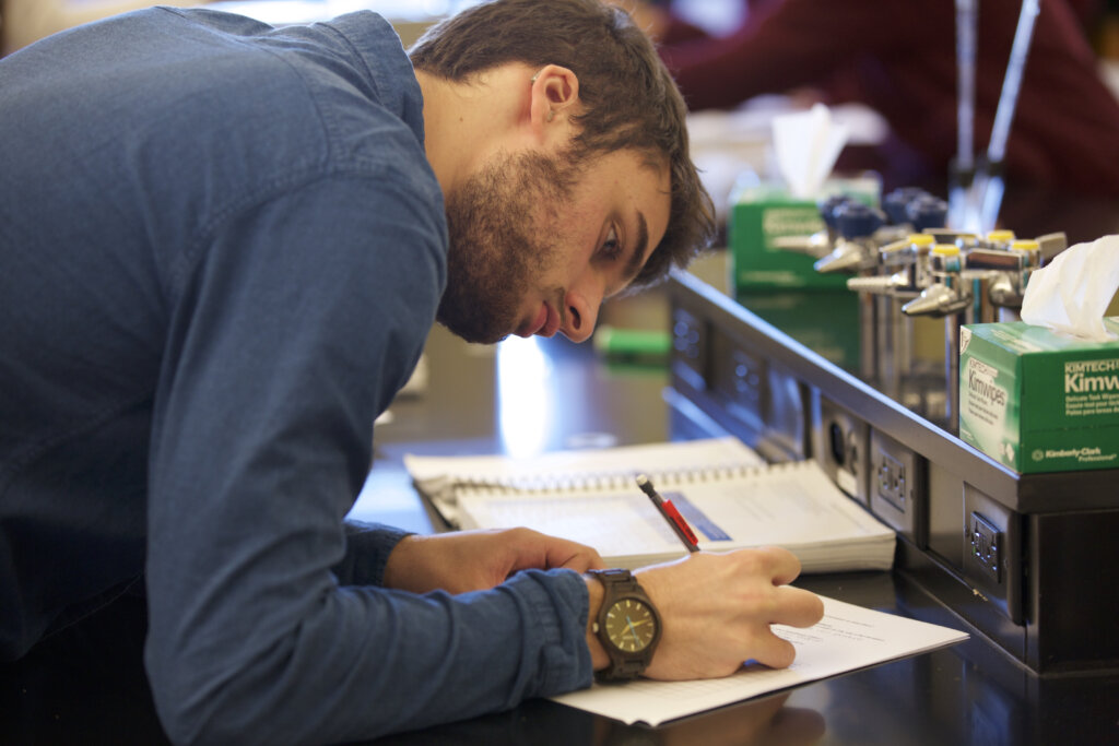 Photo of student writing in a notebook on a lab countertop.