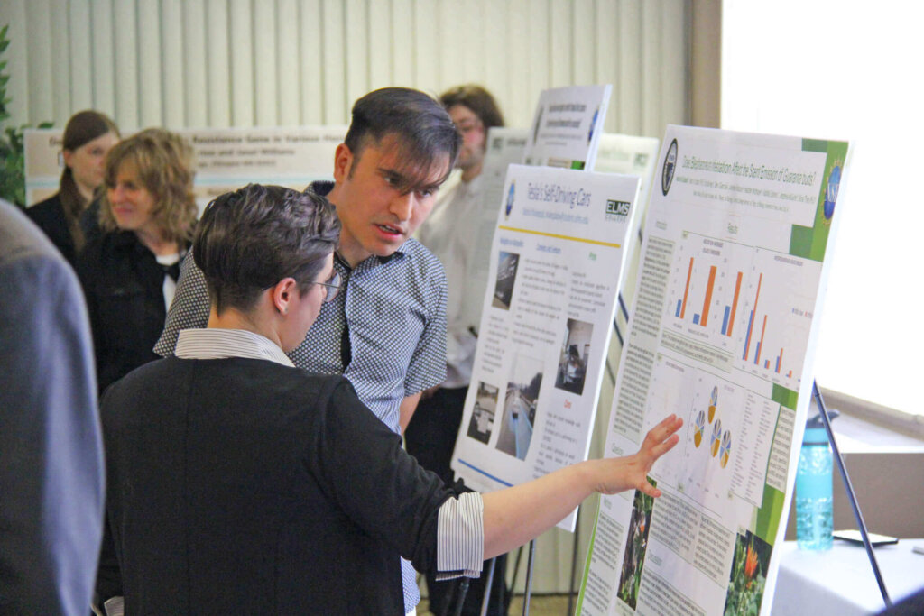 Student showing off their research from an easel.