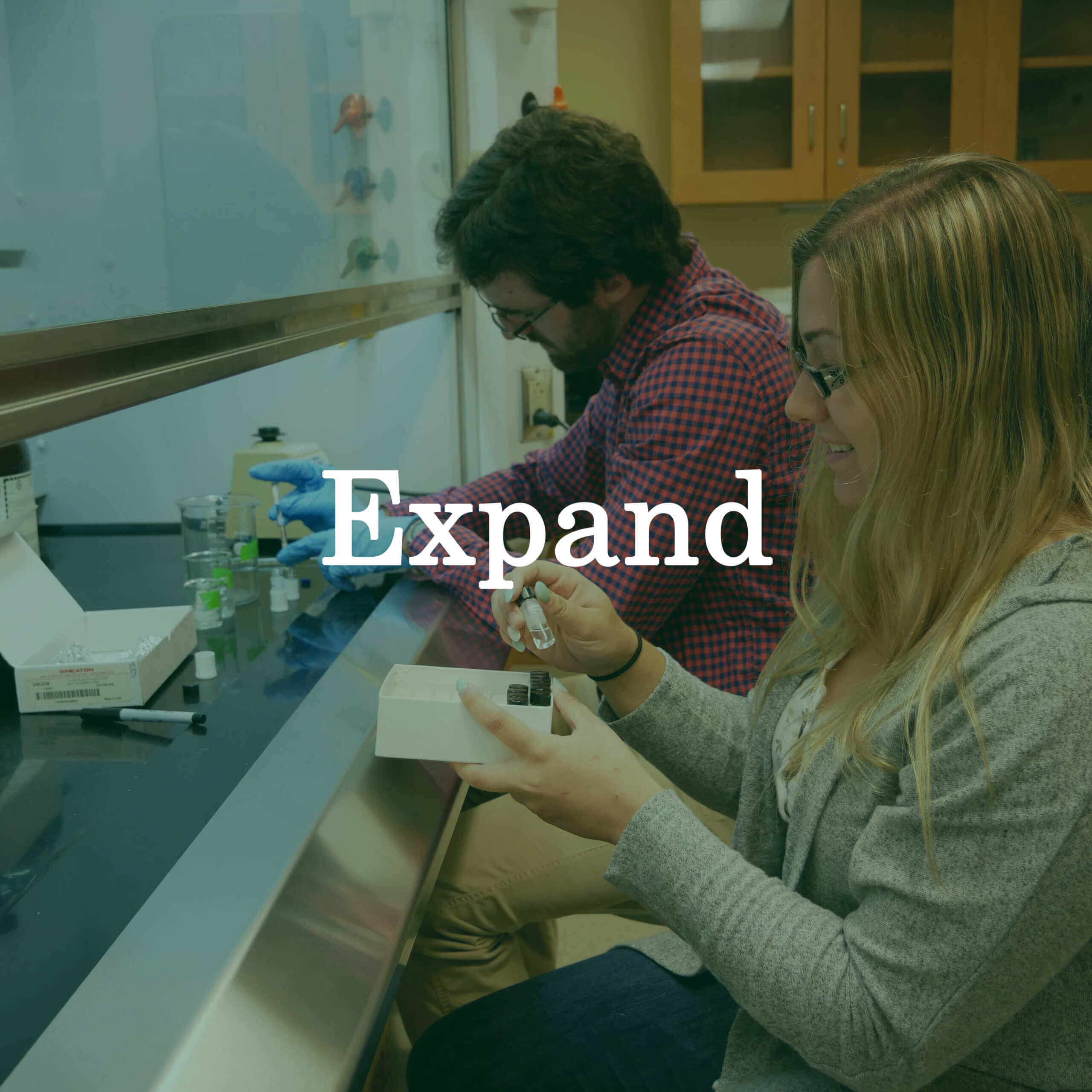 Photo of students working at a lab bench with a text overlay that reads "Expand."