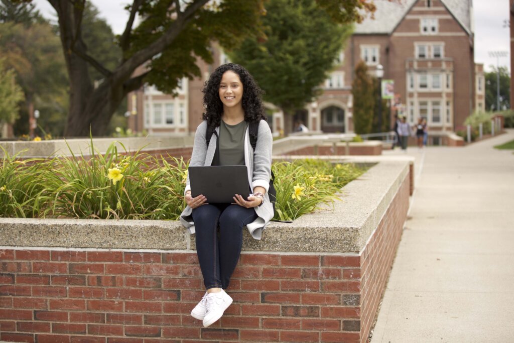 student sitting with a laptop, on a brick wall, in the quad area of campus
