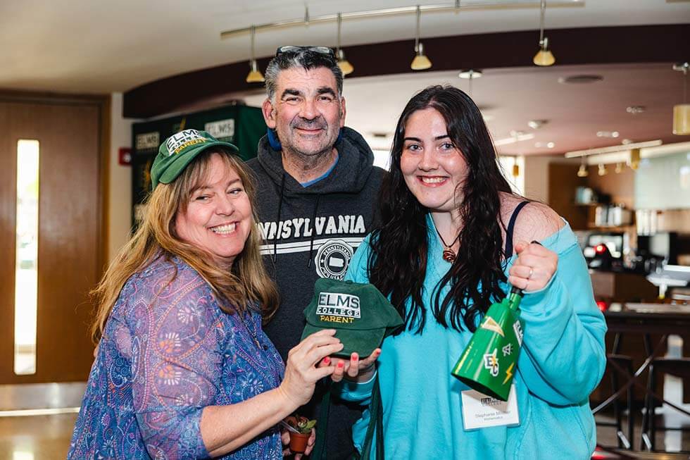 Photo of a female student and her parents, holding Elms merchandise