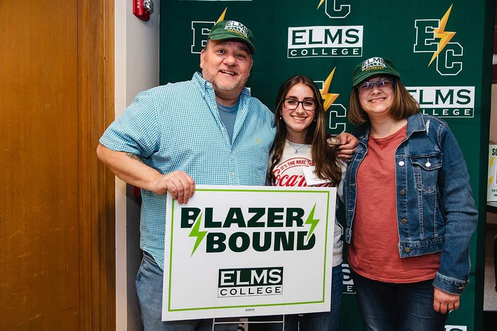 Photo of a student and her parents, parents holding a "Blazer Bound" lawn sign
