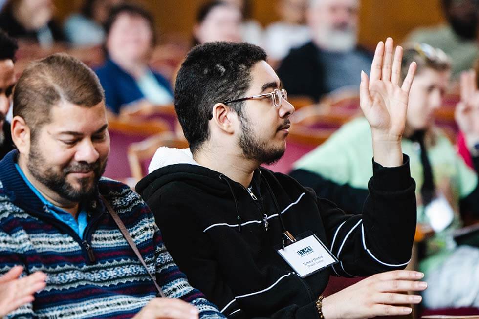 Photo of male student raising his hand sitting in Berchmans Hall, Veritas Auditorium