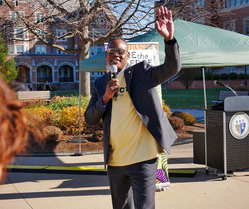 Photo of Dr. Dumay waving, holding a microphone