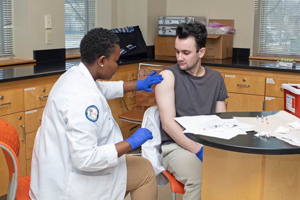 Photo of a woman giving a man a shot in the arm in an office space