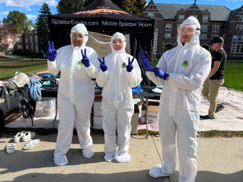 Three students in coveralls outside a paint event