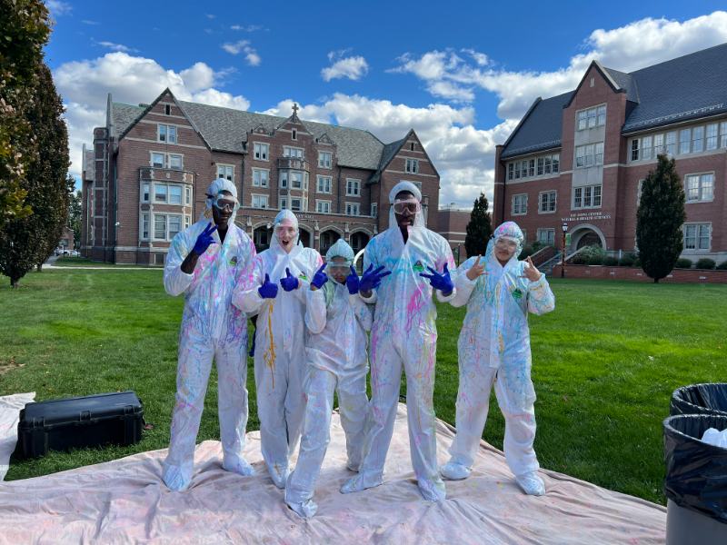 Photo of five students wearing coveralls after spray painting