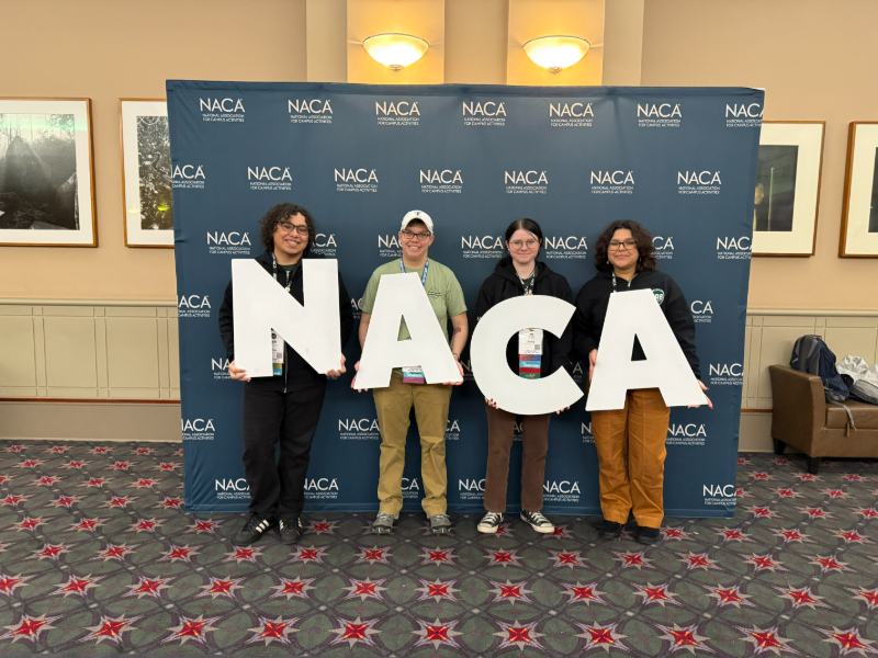 Photo of four students at an event holding up the letters N A C A