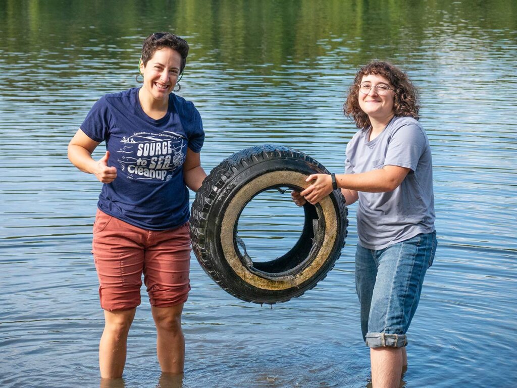 2 Elms College students holding a tire in the river