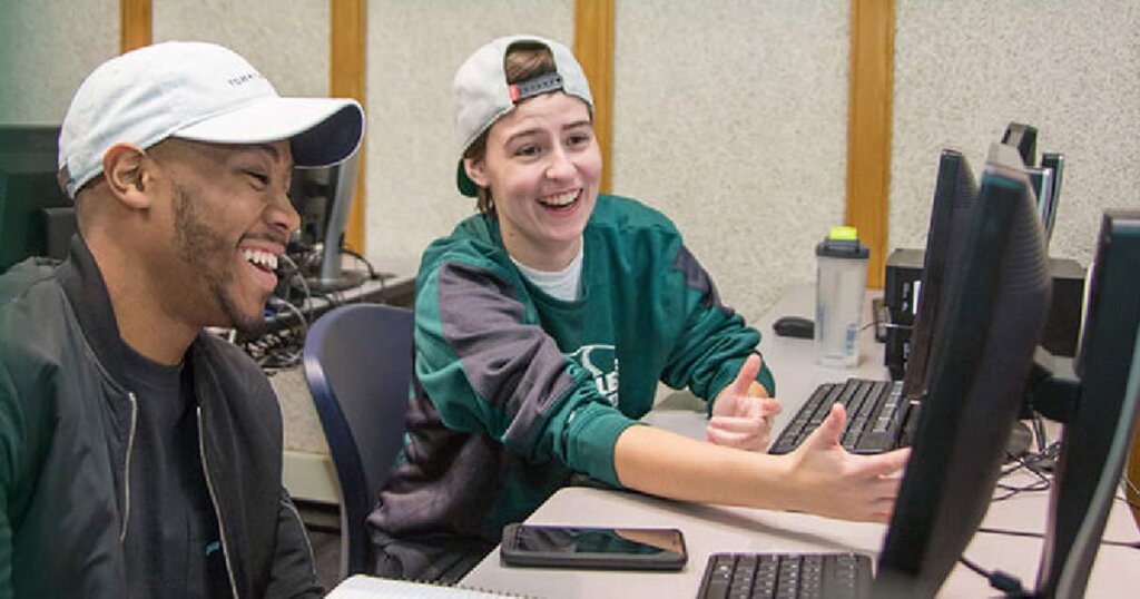 Two students in a computer lab reviewing a lcd screen